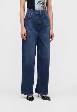 Femme portant un jean bleu foncé taille haute à jambes larges, associé à des talons noirs à bouts pointus et un t-shirt noir avec un motif de chien.