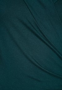 Turkusowa dzianina o gładkiej fakturze, z falującym krojem i delikatnymi zakładkami, tworzącymi płynny efekt.