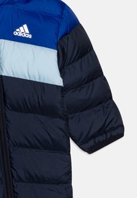 Giacca imbottita blu navy e azzurro chiaro con zip frontale, caratterizzata da sezioni orizzontali trapuntate e un logo Adidas sul petto.