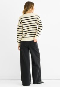 Gestreifter Strickpullover in Schwarz und Creme, mit lockerer Passform und gerippten Bündchen, kombiniert mit hoch taillierten, schwarzen Weitbeinjeans.