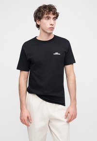 Μαύρο βαμβακερό t-shirt με κοντά μανίκια, λαιμόκοψη στρογγυλή, με λευκό κείμενο «OBEY WORLDWIDE» στο αριστερό μέρος του στήθους. Απλός σχεδιασμός, άνετη εφαρμογή.