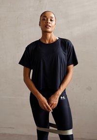 Svart cropped treningst-skjorte med korte ermer, kombinert med svarte leggings med en hvit logo. Grå motstandsbånd rundt lårene.