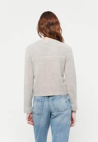 Lys grå genser med rund hals, ribbet kant og lange ermer. Myk tekstur med et minimalistisk design, som har en subtil linjedetalj.