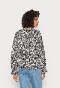 Blusa de manga longa com padrão floral em azul, laranja e branco sobre um fundo preto; apresenta punhos com babados e detalhe nas costas.
