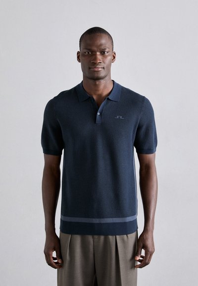 Polo de color azul marino oscuro con mangas cortas, tejido texturizado, cuello abotonado y un sutil acento a rayas en la parte inferior.