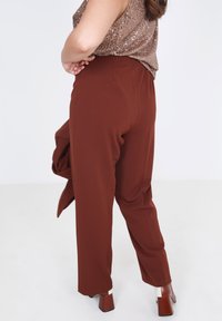 Bruine broeken met een losse fit en een elastische tailleband, gemaakt van een glad materiaal. Gecombineerd met een bronzen top met pailletten en schoenen met blokhak.