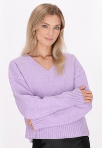 Lavendelfarbenes Strickpullover mit V-Ausschnitt, gerippten Bündchen und Saum. Weiche Textur mit lockerem Schnitt, der eine glatte Stoffoberfläche zur Geltung bringt.