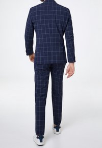 Navy checkered suit jacket and pants with white grid pattern, made from smooth fabric. Paired with white sneakers.