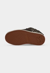 Semelle d'une basket noire avec un motif de bande de roulement en caoutchouc marron, affichant un logo de marque et un design de grip texturé.