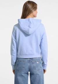 Felpa blu chiaro, accorciata, con un ampio cappuccio e polsini a costine. Abbinata a jeans in denim a vita alta con un logo triangolare sulla tasca posteriore.