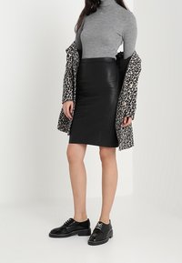 Schwarzer Leder-Bleistiftrock kombiniert mit einem grauen Rollkragenpullover und einem Leopardenmuster-Mantel. Schwarze Schnürschuhe runden das Outfit ab.