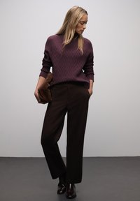 Maglione a coste color granata con motivo a spina di pesce abbinato a pantaloni a vita alta marrone scuro e borsa a mano marrone, indossato con stivaletti.