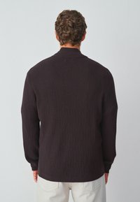 Donker gebreide trui met een ruitpatroon, geribde kraag en manchetten, een soepele textuur en een relaxte pasvorm, gecombineerd met lichtgekleurde broek.