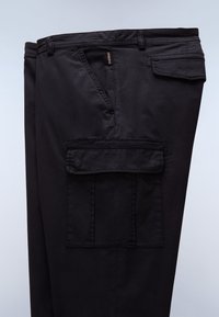 Pantalon cargo noir avec poches latérales à rabat, passants de ceinture et une petite étiquette de marque près de la couture de la poche supérieure.