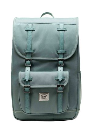 Sac à dos rectangulaire de couleur bleu sarcelle avec rabat et poche avant, sécurisé par deux sangles en cuir avec boucles en métal. Petite poignée en haut.