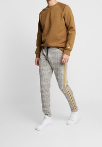 Brun sweatshirt med rund hals, kombinerad med grå rutig byxor med orangea sidostrippar och vita sneakers.