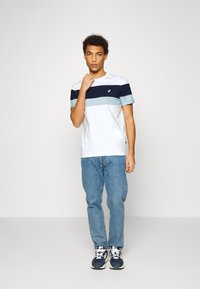 Kortermet bomull t-skjorte med horisontale striper i marineblått, lyseblått og hvitt, kombinert med lyseblå jeans og mørke sneakers.