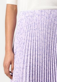 Fustă pliată dintr-un material lavandă deschis, cu un model floral complicat în violet închis. Textură fină, design până la genunchi cu o strălucire subtilă.