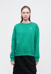 Grønn bomullssweater med ribbestrikket rund hals og mansjetter. Har en hvit Jumpman-logo på brystet. Kombinert med et svart lagdelt skjørt.