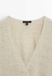 Beige knit sweater with a V-neck design, made of soft, textured fabric. Tag visible with brand and size information.
