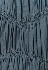 Tessuto blu con texture arricciata e cuciture elastiche che creano un motivo a zigzag. Materiale morbido e leggero con una finitura liscia.