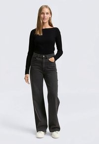 Black long-sleeve top paired with high-waisted, wide-leg, dark gray jeans. Model wears white sneakers; top features a square neckline.