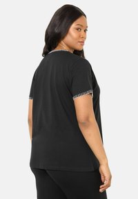 Černé bavlněné tričko s krátkým rukávem, které má bílé švy na manžetách a výstřihu. Volný střih s hladkou texturou.