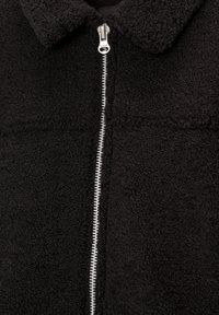Veste en polaire noire avec un col et une fermeture éclair centrale argentée. La texture semble douce et pelucheuse avec une couleur uniforme.