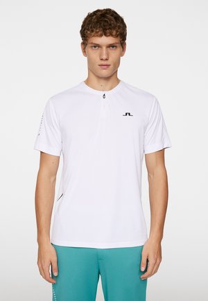 Hvid kortærmet t-shirt med rund hals, lynlåsdetalje, sort logo på brystet og kontrasterende sort accent nær sidesømmen.