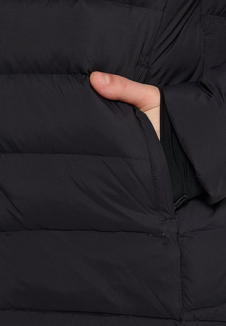 Schwarze Pufferjacke mit horizontalen Steppnähten. Eine Hand befindet sich in einer Seiten Tasche, wodurch die Textur des Stoffes und die Nahtdetails zur Geltung kommen.