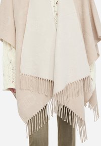 Sciarpa beige con bordi frangiati, caratterizzata da una texture morbida e un delicato motivo a logo in rilievo. Leggera e si drappeggia in modo elegante.