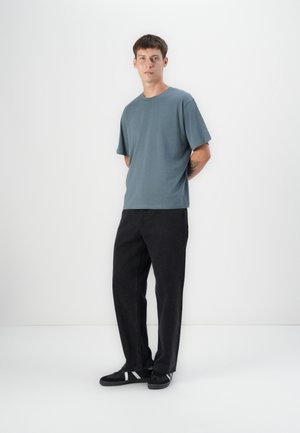 Camiseta de algodón de color azul claro con un corte relajado, combinada con pantalones de mezclilla negros. El modelo lleva zapatillas negras con acentos blancos. Diseño sencillo y moderno.