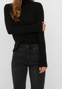 Pull en laine à col roulé noir côtelé associé à un jean ajusté gris foncé. Le pull possède des manches longues avec des poignets prolongés et un design près du corps.