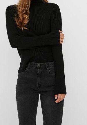 Černý žebrovaný rolák v kombinaci s tmavě šedými přiléhavými džíny. Svetr má dlouhé rukávy s prodlouženými manžetami a těsný střih.