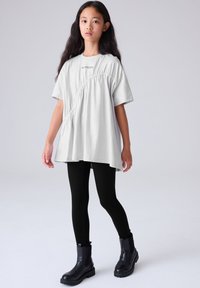 Svijetlosiva široka majica s nabranim detaljem sa strane, kratkim rukavima i logotipom. Kombinirana s crnim helankama i crnim čizmama do gležnja.