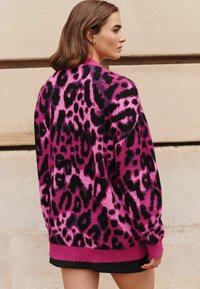 Per didelį megztinį rožinės ir juodos leopardo rašto, megztas tekstūros, su juostelėmis rožinės spalvos apačioje ir rankogaliuose. Dėvima virš juodos maikutės.