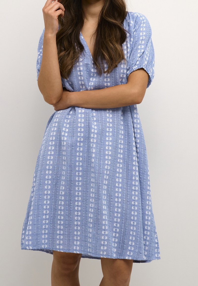 Blå klänning med V-ringning, korta puffärmar, blommönster och en flödande design med texturerade ränder. Tillverkad av bomull.