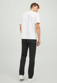 White cotton t-shirt with short sleeves, paired with black pants and white sneakers. The back of the outfit is visible, with a plain design.