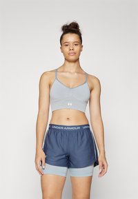 Sostén deportivo gris claro con mezcla de spandex, con tirantes finos y un diseño texturizado. Pantalones cortos azul marino con una cinturilla gris claro y un logo.