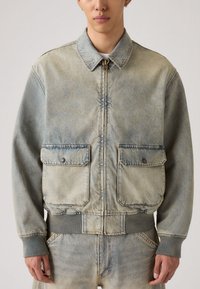 Τζιν μπουφάν σε ανοιχτό μπλε χρώμα με φερμουάρ, δύο μπροστινές τσέπες, ριμπ μανσέτες και ζώνη μέσης. Υφή με ελάχιστο ξεθώριασμα.