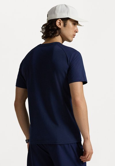 Ναυτικό μπλε αθλητικό μπλουζάκι με κοντά μανίκια, λεία υφή και στρογγυλή λαιμόκοψη, φορεμένο με λευκό καπέλο που έχει διάτρητες λεπτομέρειες.