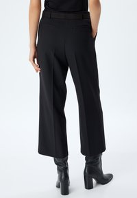 Pantalons noirs cropped avec une coupe droite, dotés de poches arrière et d'une texture lisse. Associés à de hautes bottes à talons noires.