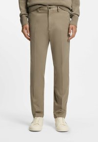 Beige Chino-Hosen aus leichtem Stoff, mit glatter Textur und französischen Taschen, kombiniert mit weißen Sneakern.
