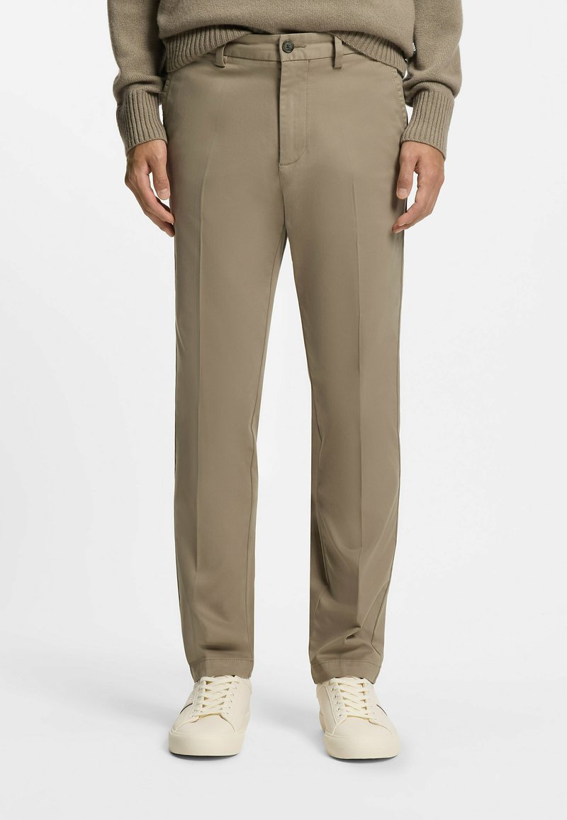 Beige Chino-Hosen aus leichtem Stoff, mit glatter Textur und französischen Taschen, kombiniert mit weißen Sneakern.
