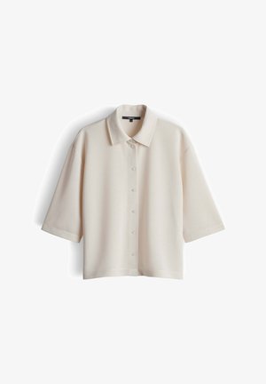 Camicia a maniche corte color crema con bottoni e colletto appuntito, mostrata distesa su uno sfondo bianco.