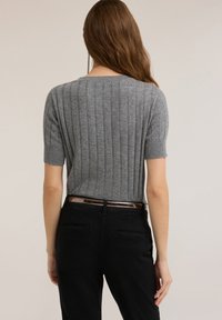 Suéter gris de manga corta con tejido acanalado y cuello redondeado, combinado con pantalones negros que tienen un cinturón brillante y bolsillos traseros.