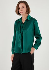 Emerald green satin blouse with a collar, long sleeves, and button details. Features a loose fit and smooth texture.