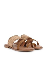 Sandalias marrones con dos correas trenzadas anchas y un bucle para el dedo del pie. El material es una mezcla de suave ante y tejido trenzado texturizado. Suela plana.