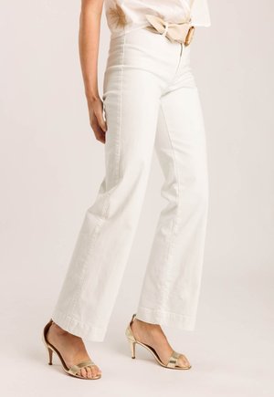 Witte wijde jeans met een soepele textuur, gedragen met gouden hoge hakken. Heeft een hoge taille en subtiele voorzakken.