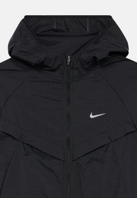 Čierna vetrovka Nike s kapucňou, predným zipsom a bielym logom Nike swoosh na hrudi.
